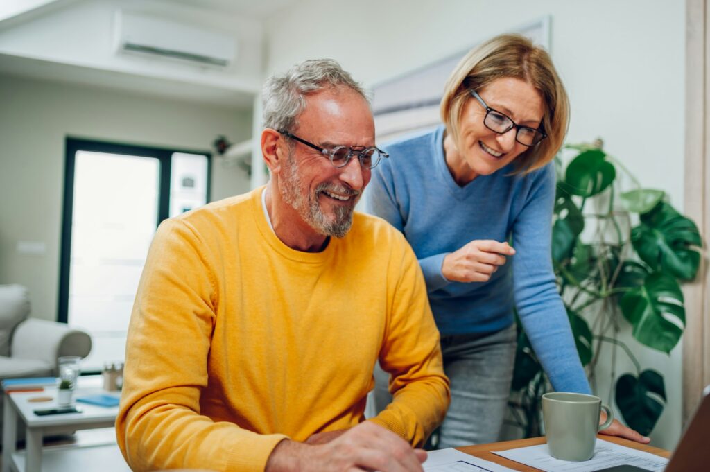 Senior middle aged happy couple using laptop together at home.